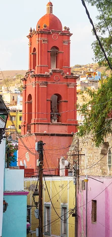 Vista de una torre de iglesia color rojo vibrante y casas coloridas en un pueblo tradicional de México, representando los destinos de entrega de Ágilex.