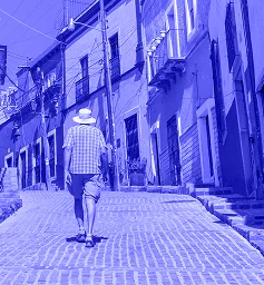 A man walking down a cobblestone street lined with traditional architecture, rendered in a monochromatic blue tone, symbolizing Ágilex's presence in Mexico and the ease of sending and receiving international payments from Colombia.