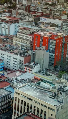 Vista aérea de edificios comerciales y residenciales en una zona urbana de México, destacando un edificio rojo moderno, representando la infraestructura de rutas propias para envíos internacionales de Ágilex.
